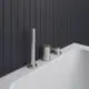 Drei-Loch Wannenrandarmatur von Ideal Standard in Silber mit Handbrause und Umsteller, montiert auf einer weißen Badewanne vor schwarzen Fliesen.